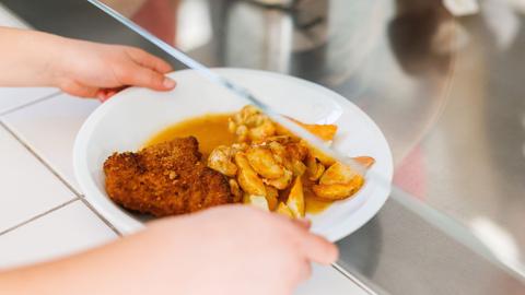 Eine Grundschülerin nimmt einen Teller mit Schnitzel, Kartoffeln und Sauce.