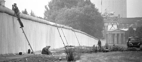 Grenzsoldaten der DDR sitzen hinter der Berliner Mauer.