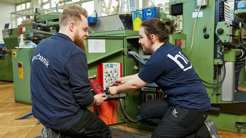 Auszubildende und Ausbilder in der Mechanik arbeiten an einer Maschine