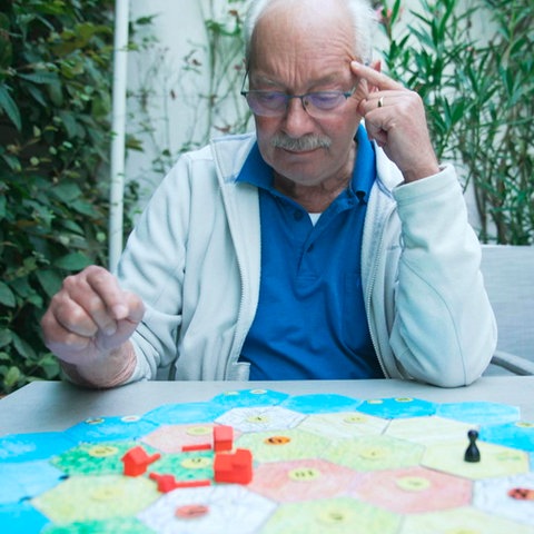 Spieleerfinder Klaus Teuber sitzt am Tisch vor dem Spielfeld seines Welterfolgs "Catan".