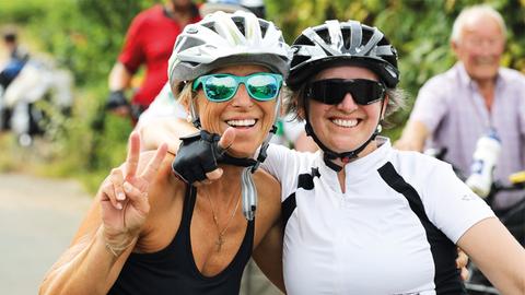 Zwei Radfahrerinnen lächeln gut gelaunt in die Kamera