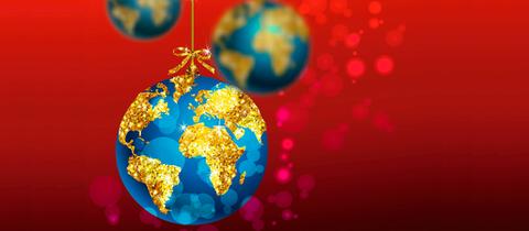 Blaue Weihnachtsbaumkugel mit goldener Weltkugel vor rotem Hintergrund