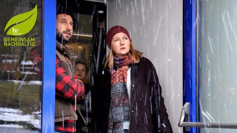 Familie (Vater, Mutter, dahinter Kind) schauen aus dem Eingangsbereich einer Tür hinaus in den dichten Graupelregen. Filmszene mit Serkan Kaya, Katja Studt