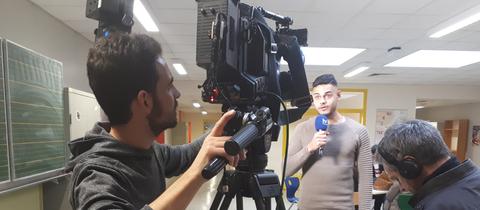 Ein Schüler filmt mit einer Kamera einen anderen Schüler, der in ein Mikrofon spricht.