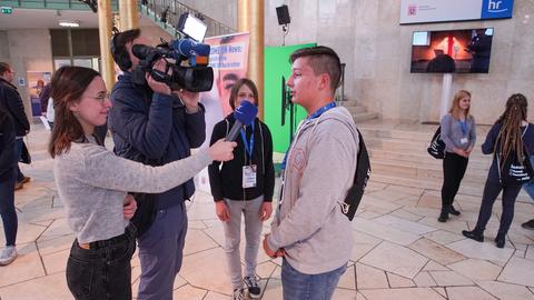 In der Goldhalle des Hessischen Rundfunks interviewt eine Schüler-Reportertin einen teilnehmenden Schüler vor der Kamera.