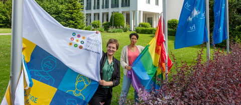 Diversity-Beauftragte Sinaida Thiel (links) und Hadija Haruna-Oelker vom Diversity-Team des hr hissen die Flagge der "Charta der Vielfalt" und die Regenbogenflagge vor dem Funkhaus in Frankfurt