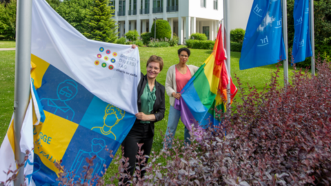Diversity-Beauftragte Sinaida Thiel (links) und Hadija Haruna-Oelker vom Diversity-Team des hr hissen die Flagge der "Charta der Vielfalt" und die Regenbogenflagge vor dem Funkhaus in Frankfurt