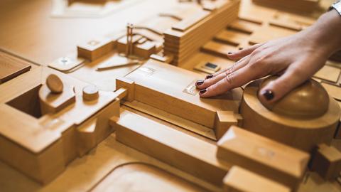 Ein aus Holz gefertigter taktiler Lageplan mit den Gebäuden des hr, dazu Beschriftung in Braille. In Großaufnmahme eine Hand, die fühlt.