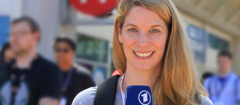Katharina Wilhelm hält ein Mikrofon in der Hand und steht auf der Straße