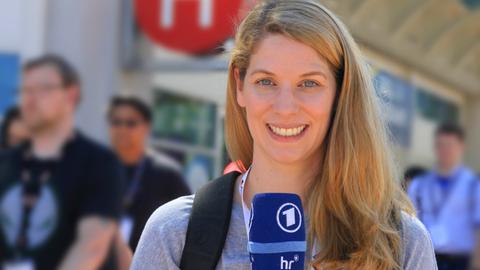 Katharina Wilhelm hält ein Mikrofon in der Hand und steht auf der Straße