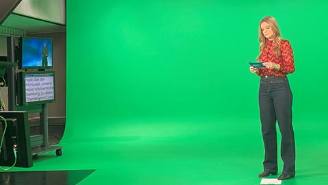 Eine Moderatorin steht in einem TV-Studio vor einer grünen Wand.