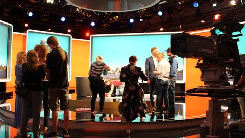 Zwischen den Aufnahmen geht es im Studio hektisch zu: Die Maske kontrolliert das Make-up, das Kostüm den Sitz der Kleidung, der Regisseur spricht mit den Schauspielern.