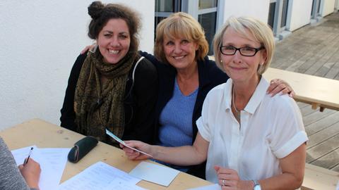 Die hr-Mitarbeiterinnen Astrid Sic und Maria Stähle sitzen mit einer Komparsin auf einer Bank.