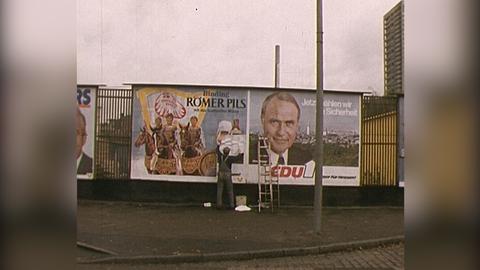 Mann überklebt Plakate auf einer Plakatwand