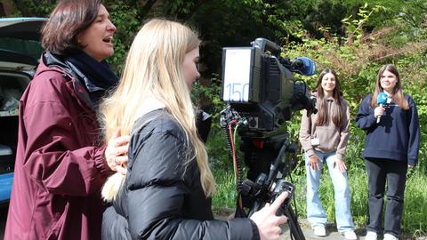 Szene im Freien auf dem hr-Gelände: Ein Mädchen steht an einert Kamera auf Stativ, deneben eine heöfende hr-Mitarbeiterin. Vor ihnen stehen zwei Mädchen mit einem Handmikrofon, bereit für das Interview. Die Mädchen sind etwa 13-15 Jahre alt.