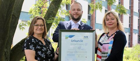 Die AfB gemeinnützige GmbH übergab eine Urkunde für das gemeinsame sozial-ökologische Wirken.  Von links: Brigitte Puchert (Materialwirtschaft), Alexander Schwander (Partner-Manager AfB) und Maike Sawinski (Leiterin Liegenschaftsverwaltung)