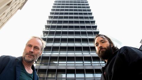 Szene aus dem hr-Tatort "Der Turm": Kommissar Paul Brix (Wolfram Koch, links) und Assistent Jonas (Isaak Dentler) vor einem riesigen Büroturm